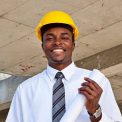 African man in a suit and construction hat holding architecture plans on site